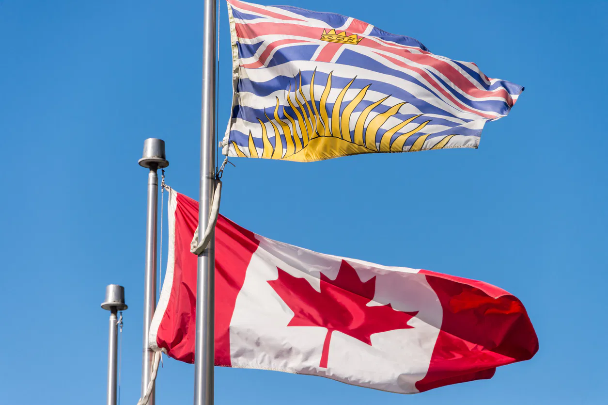 Canada and British Columbia flags waving over blue sky in Vancouver, BC, Canada